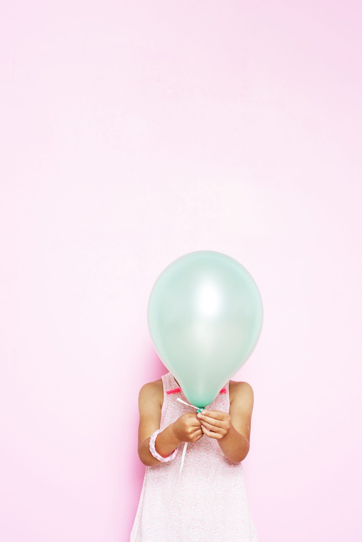 Beautiful and funny little girl covering his face with a balloon